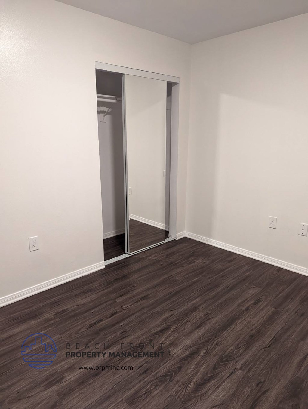 a bedroom with white walls and wood flooring and a closet